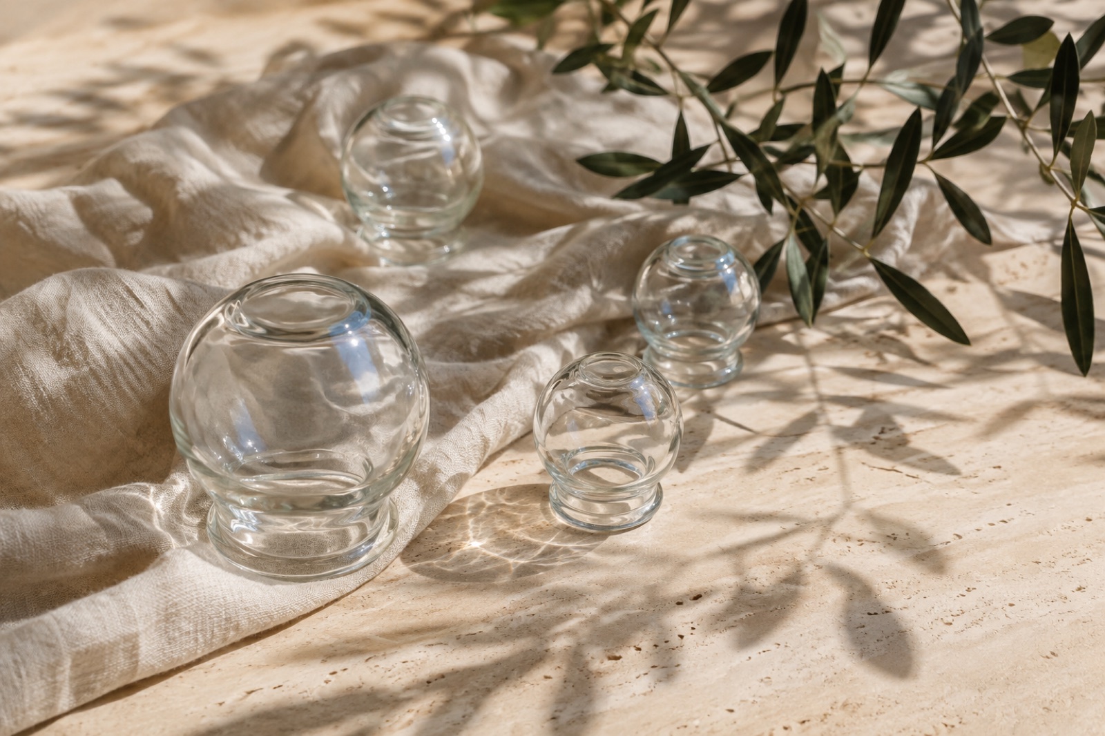 Editorial image for Cupping: glass cupping vessels on linen with olive leaves.